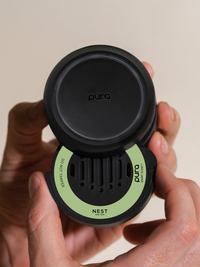 Person inserting a car fragrance into the Pura car diffuser with a beige background